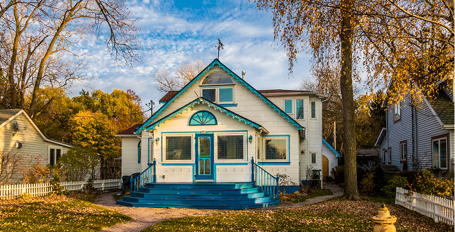 An older white house with blue trim in the fall