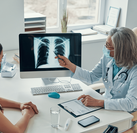 A doctor showing a patient an x-ray of their lungs at a computer desk