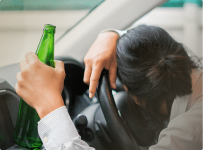 Image of a person sleeping at the wheel holding a beer bottle