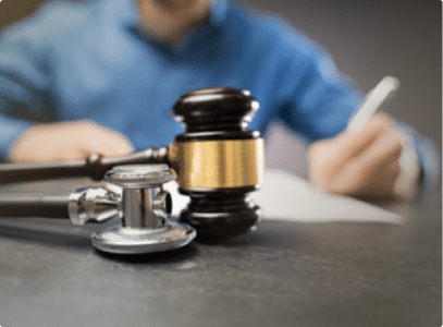 A judges gavel and stethoscope on a desk as someone fills out paperwork