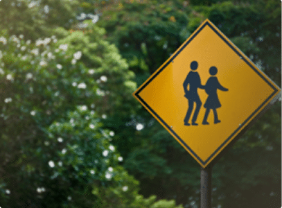 a crosswalk sign with greenery behind it