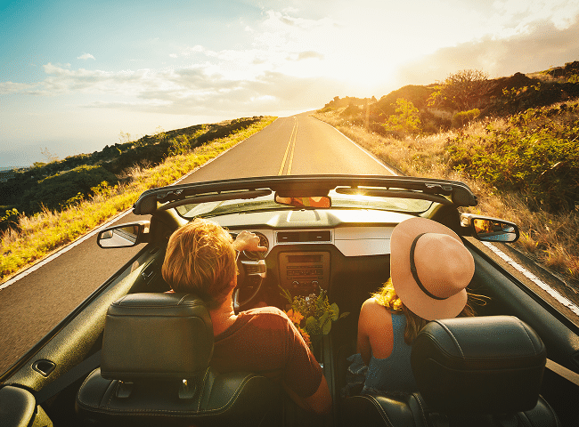 couple driving down an empty road at sunset in a convertible