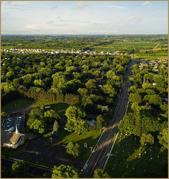 Arial shot of a small town including a church, trees, homes, and roads