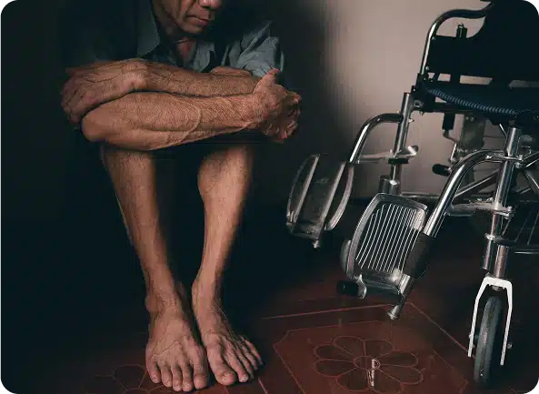 A man sitting on the ground, holding his knees next to a wheelchair