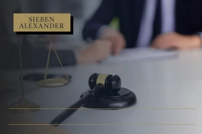 A judges desk including a gavel and a scale in front of two attorneys blurred in the back